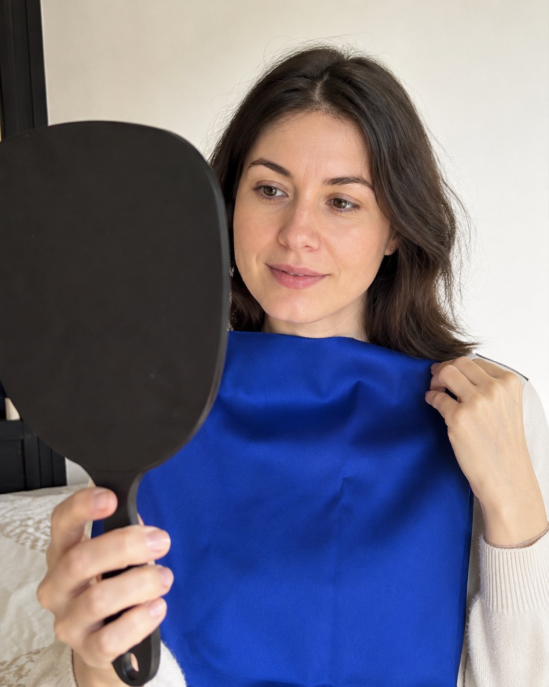 Femme tenant un tissu bleu royal près du visage et se regardant dans un miroir à main — test de draping colorímétrique